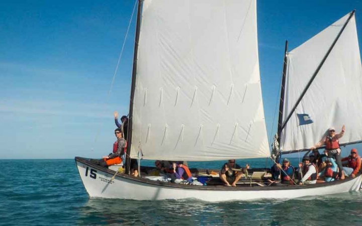 a sailboat full of people sits on calm water on an outward bound course